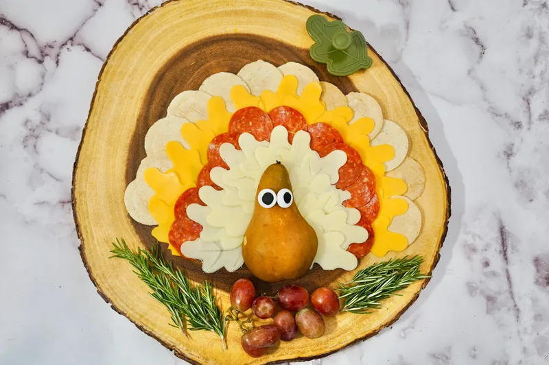 Leaf-shaped cheese and pepperoni arranged in turkey feather pattern on wooden board