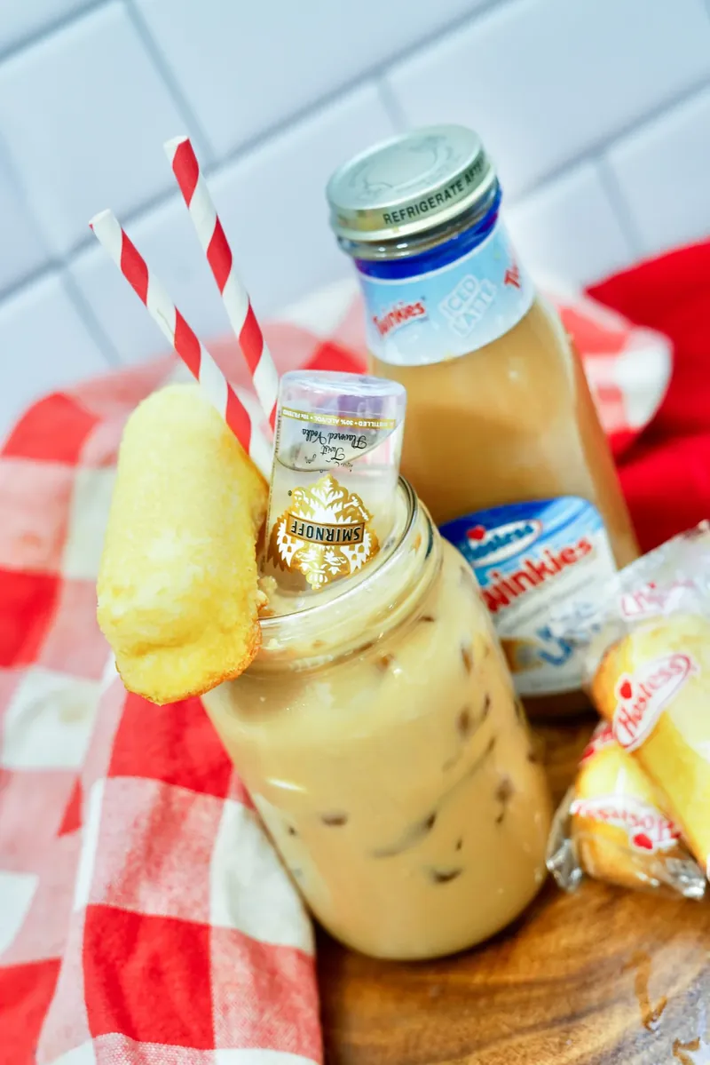 Close up of Twinkie boozy iced latte with vanilla vodka bottle and Twinkie garnish