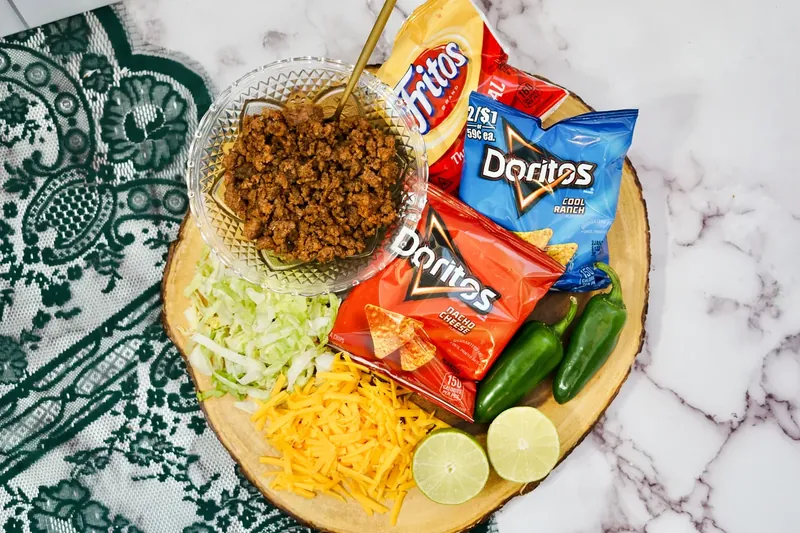 Walking taco ingredients including taco meat, cheese, lettuce, jalapeños and chip bags