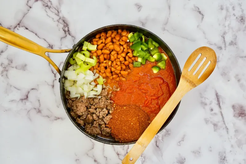 Ground beef, beans, vegetables, and spices added to large pot for chili