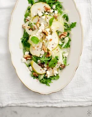 Elegant pear and arugula salad with goat cheese and walnuts on oval white platter