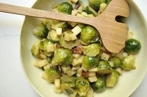 Brussels sprouts with bacon and onions in cast iron skillet with wooden serving spoon