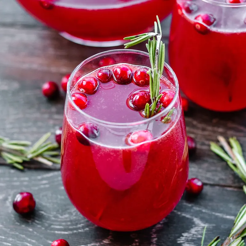 Festive cranberry punch in stemless wine glass with cranberry and herb garnish