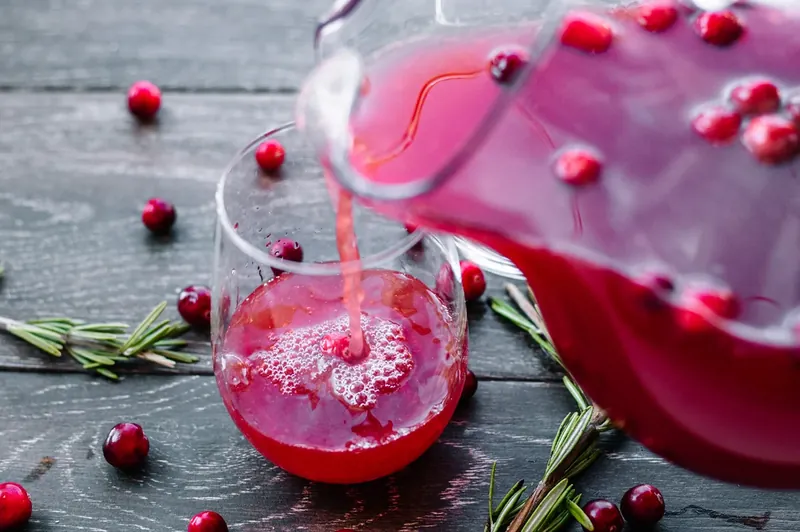 Pouring cranberry wine into glass pitcher with punch mixture and fresh cranberries
