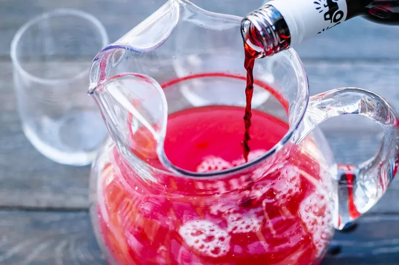 Pouring red cranberry holiday punch from pitcher into cocktail glass