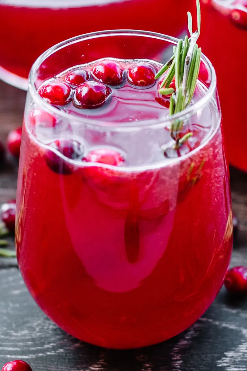 Alcoholic cranberry holiday punch in glass with fresh cranberries and rosemary garnish
