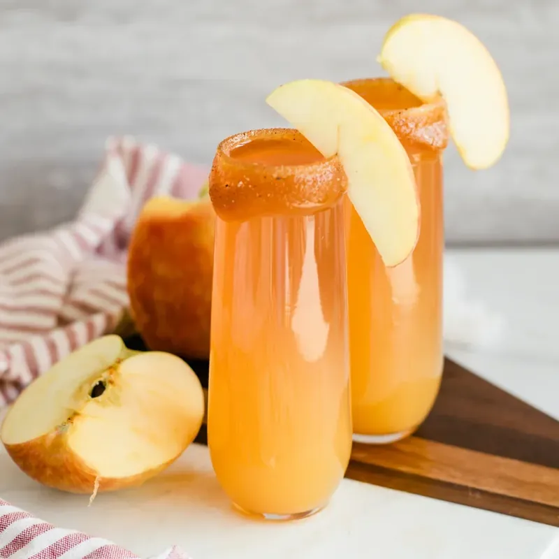 Two apple cider mimosas with caramel sugar rim and fresh apple garnish for fall entertaining