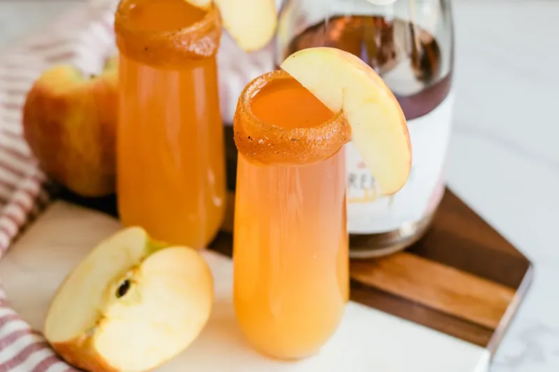 Adding apple slice garnish to completed apple cider mimosa with caramel rim
