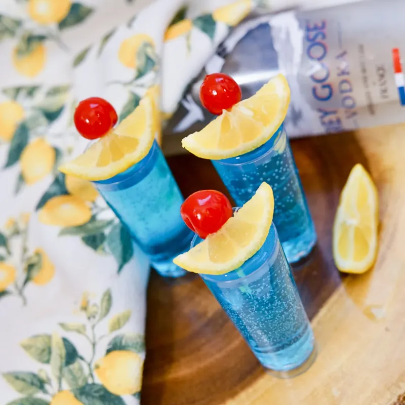 Three blue kamikaze shooters with lemon and cherry garnish ready to serve