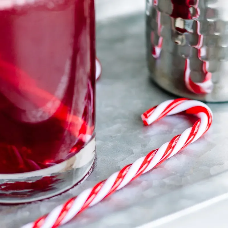 Beautiful candy cane margarita with sugar rim and festive garnishes on marble surface