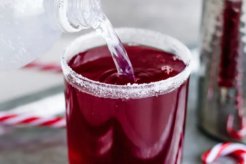 Red cranberry margarita mixture being poured into sugar-rimmed glass over ice