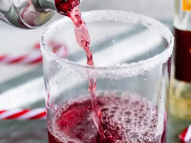 Sugar-rimmed cocktail glass being prepared with lime wedge for candy cane margarita