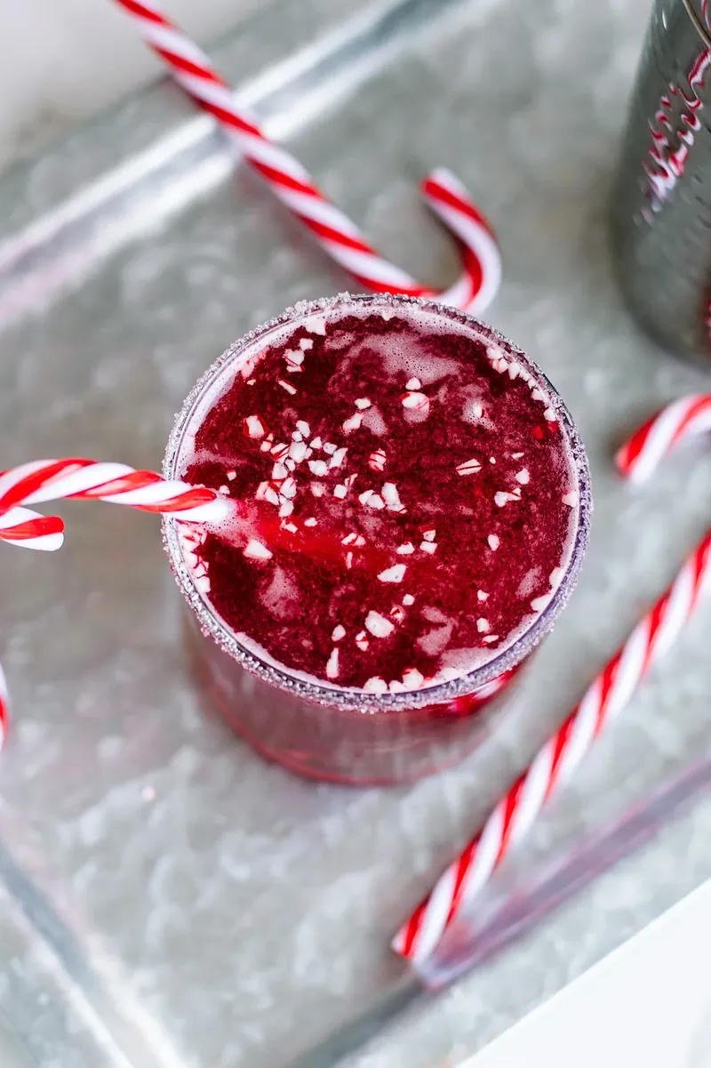 Red candy cane margarita in sugar-rimmed glass with candy cane garnish and crushed peppermint