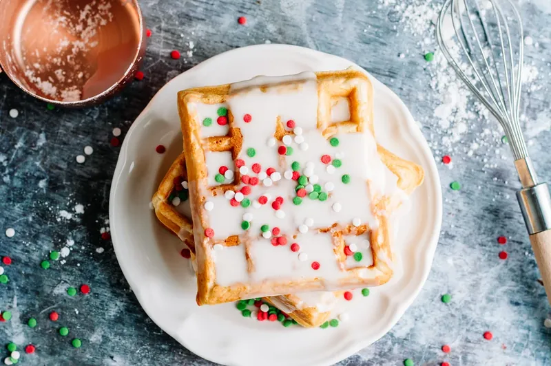 Christmas sprinkles being added to glazed waffles on white plate with red green white sprinkles