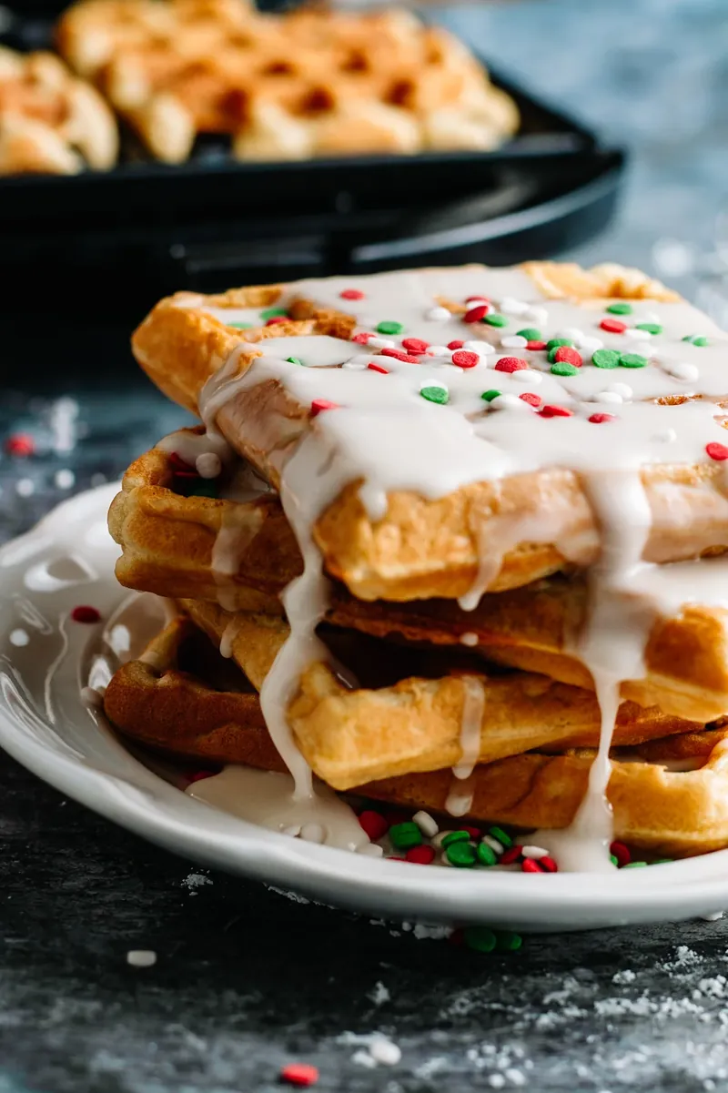 Christmas glaze donut waffles stacked on white plate with white glaze and red green sprinkles