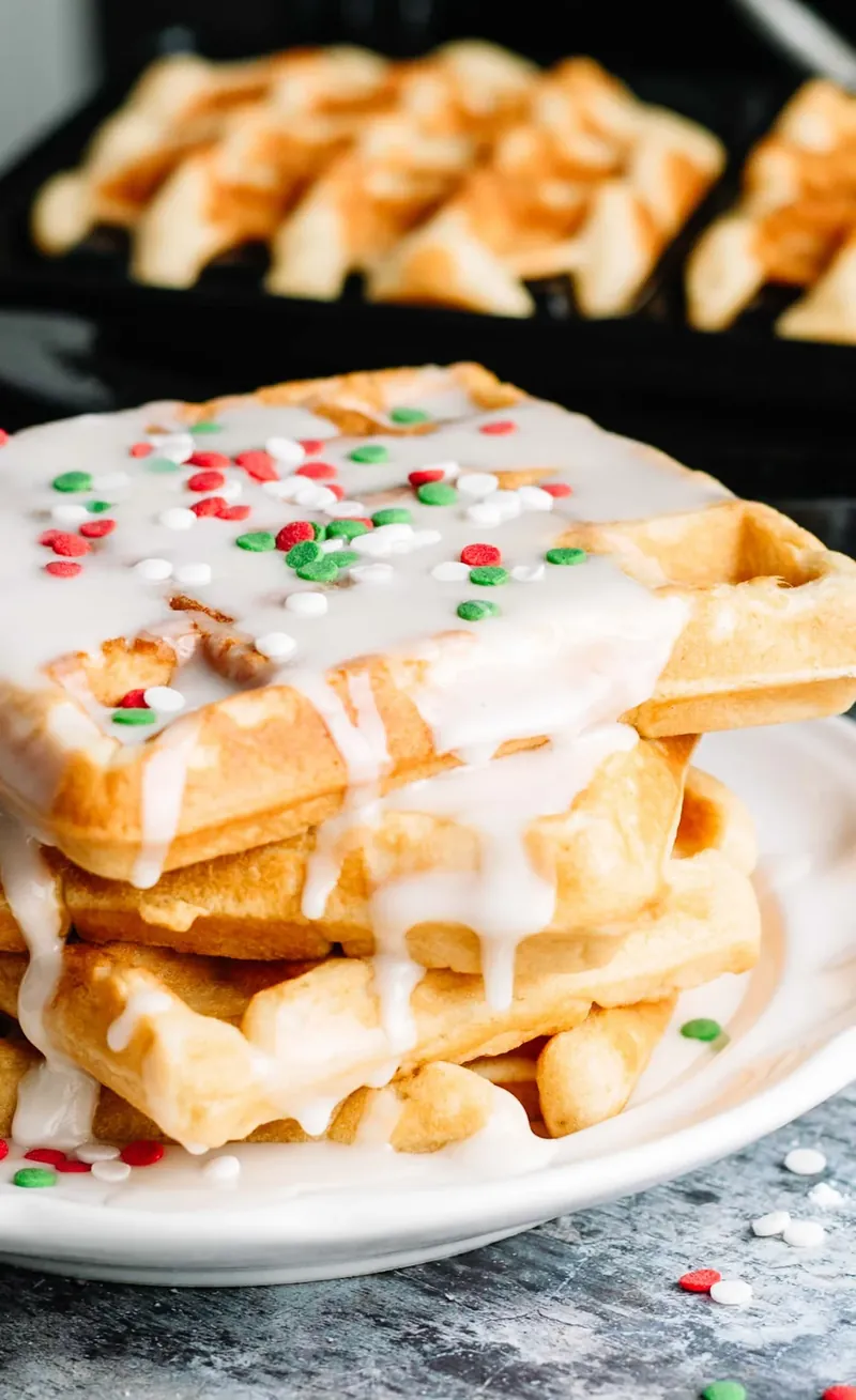 Glazed donut waffles with Christmas sprinkles on white plate next to waffle maker