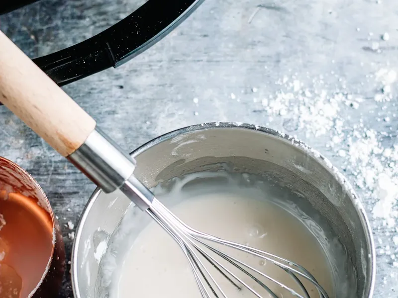 Wire whisk mixing white glaze in small bowl with powdered sugar and milk
