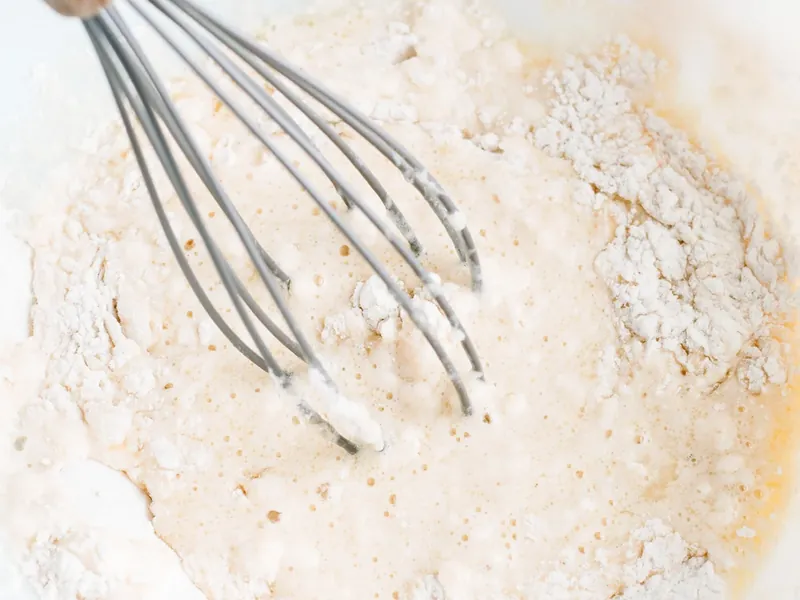 Wire whisk mixing waffle batter in white bowl showing combined wet and dry ingredients