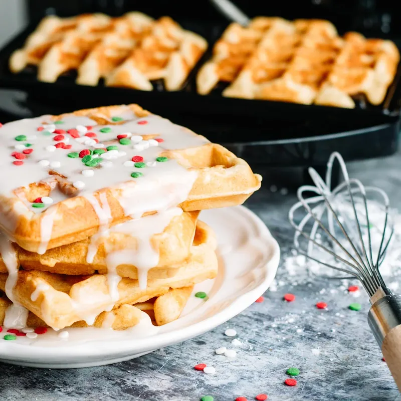 Stack of Christmas glaze donut waffles with white glaze and colorful sprinkles on white plate
