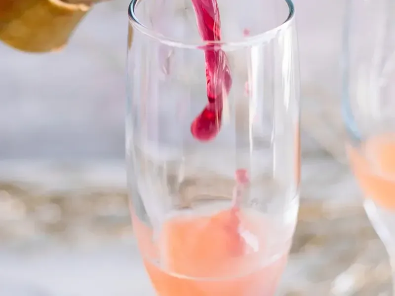 Adding cran-raspberry juice to champagne flute with grapefruit juice