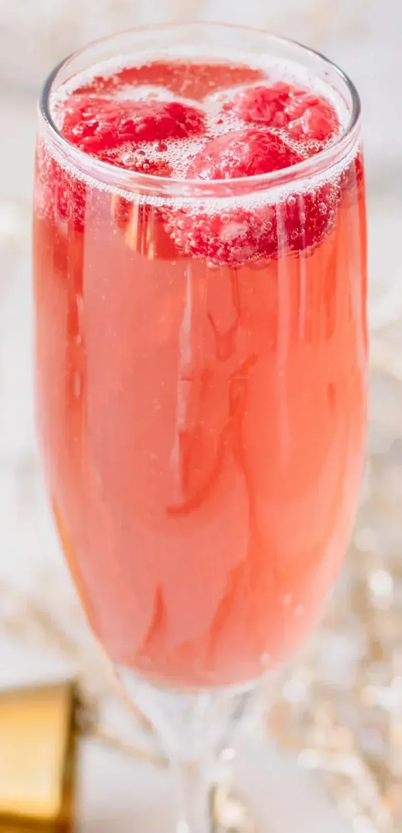 Christmas mimosa in tall champagne flute with raspberry garnish