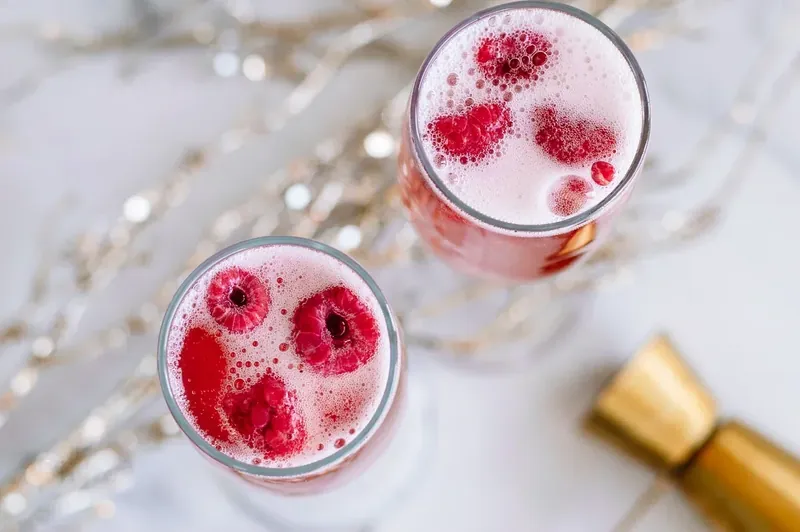 Adding fresh raspberries to completed Christmas mimosa cocktail