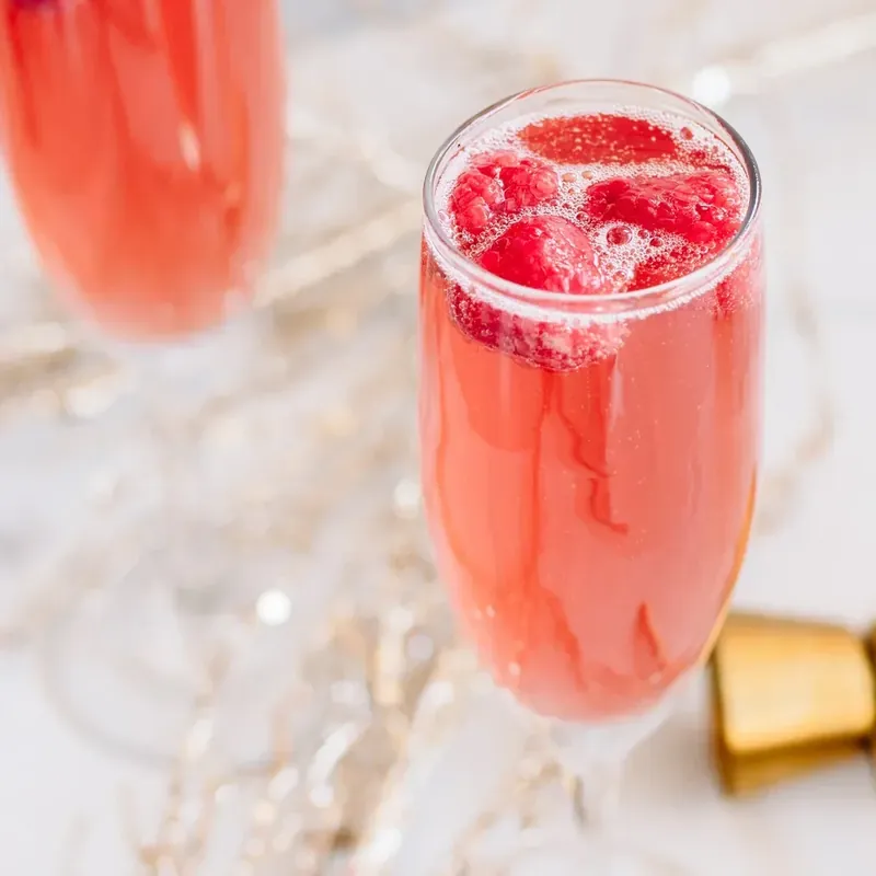 Overhead view of two Christmas mimosas with raspberries on marble surface