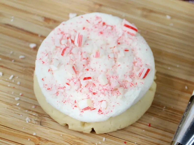 Cookie with white frosting being topped with crushed red and white candy cane pieces