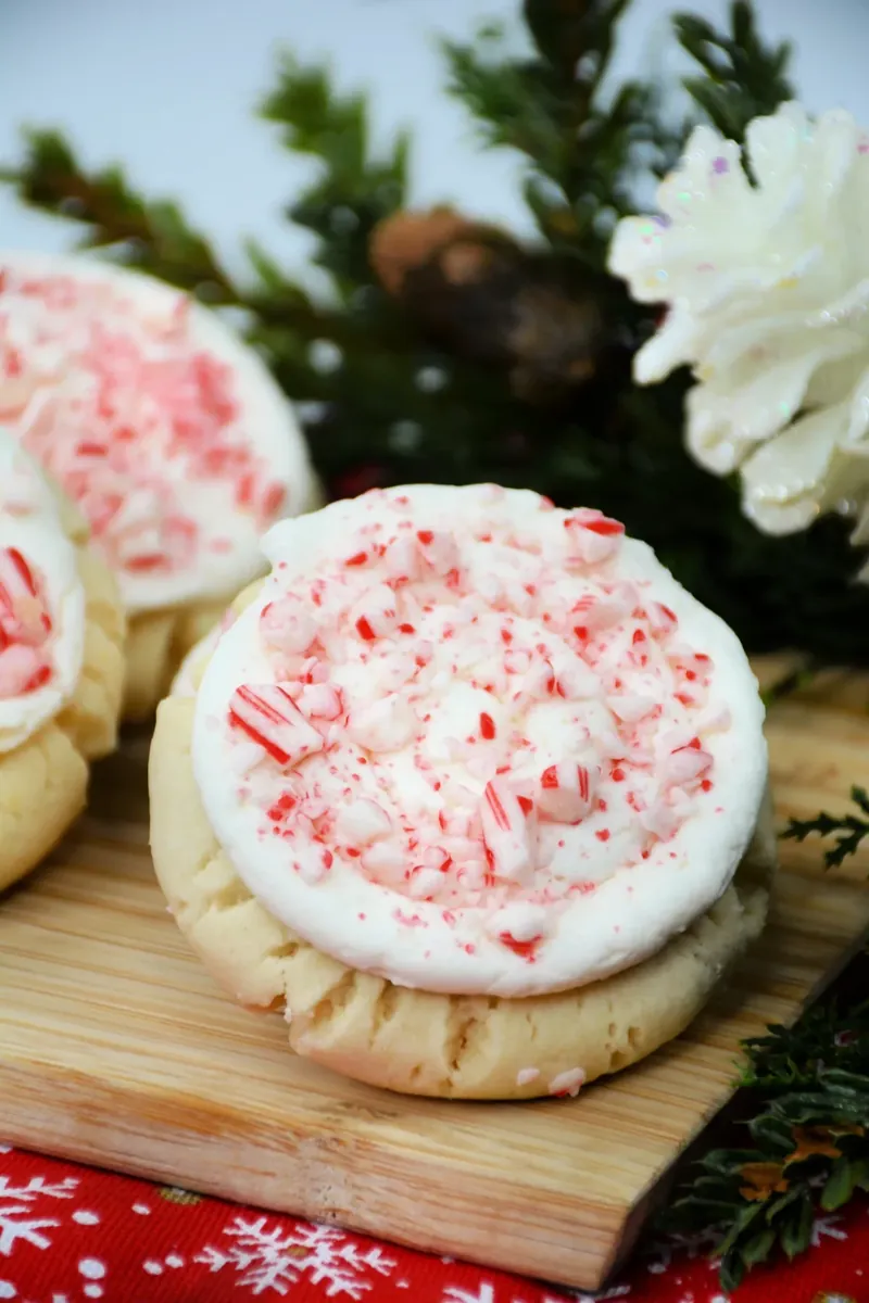 Close up of Crumbl candy cane cookie with swirled white frosting and red candy cane sprinkles on wooden board