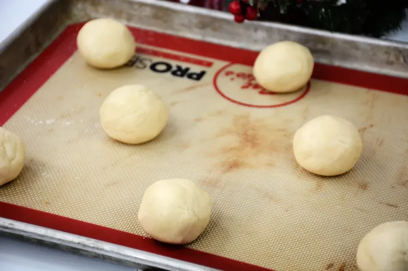 Cookie dough balls placed on silicone baking mat on sheet pan ready for baking