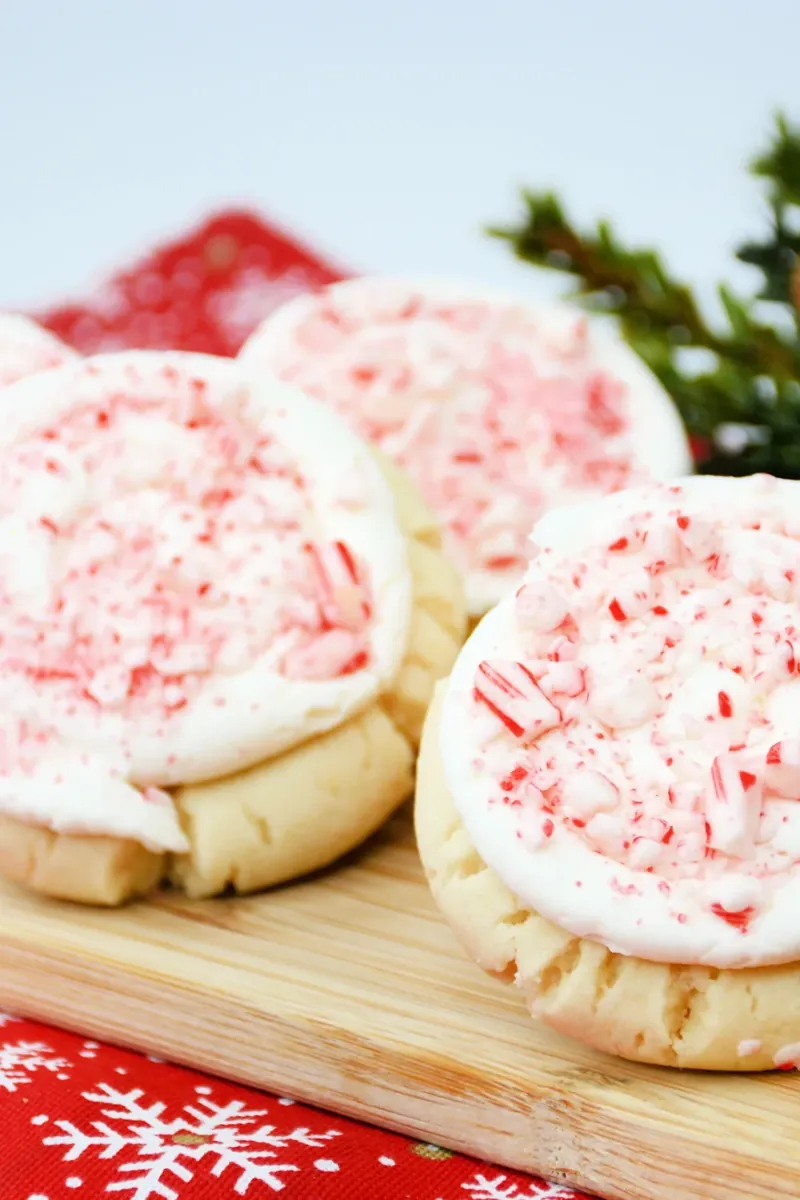 Multiple Crumbl candy cane cookies with peppermint frosting arranged on wooden board with Christmas decorations