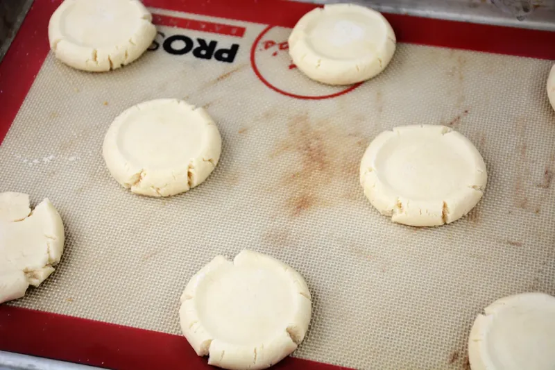 Flattened cookie dough disks on baking mat after being pressed with sugar-coated cup