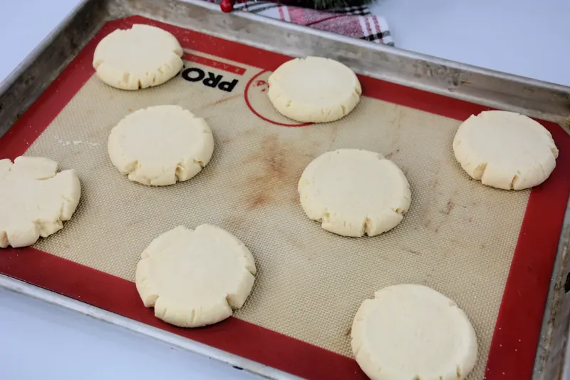 Shaped cookie dough disks on silicone baking mat ready to go into preheated oven