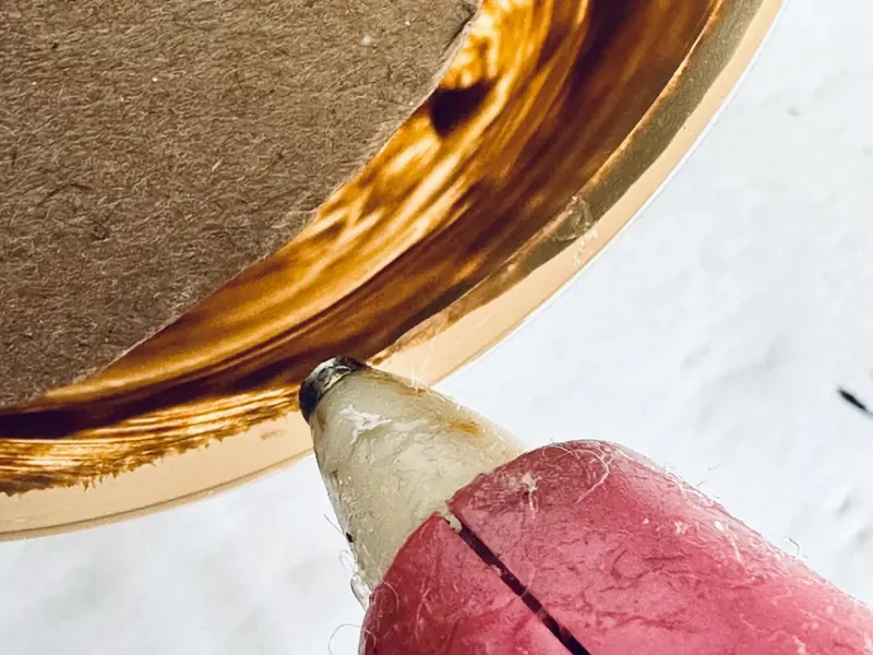 Hot glue gun applying glue to rim of painted mug with cardboard circle ready to attach