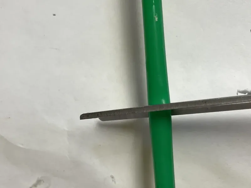 Green plastic straw being cut in half with scissors for hot cocoa mug decoration
