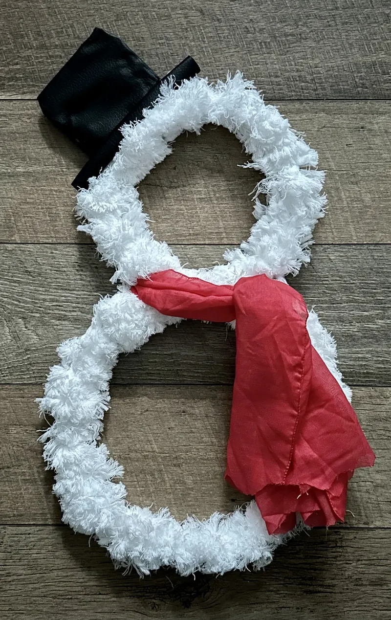 Completed Dollar Tree fluffy snowman wreath with black hat and red scarf on wood background