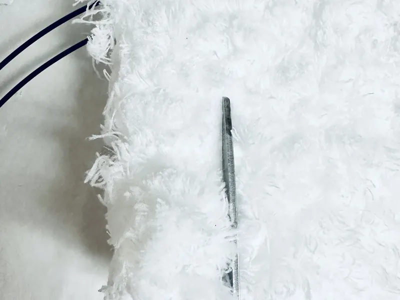 Cutting white microfiber cloth into strips with scissors for snowman wreath
