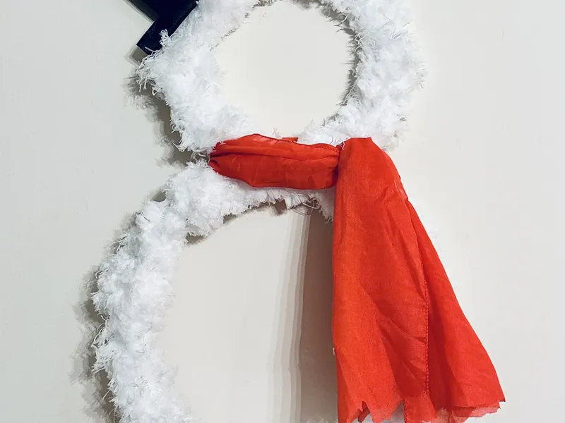 Tying red fabric scarf around neck of fluffy snowman wreath