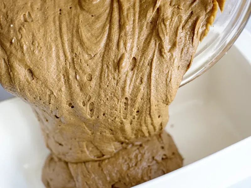 Gingerbread batter being poured from mixing bowl into greased 8x4 loaf pan