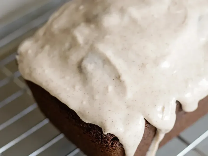 White cinnamon glaze being drizzled over gingerbread loaf on cooling rack