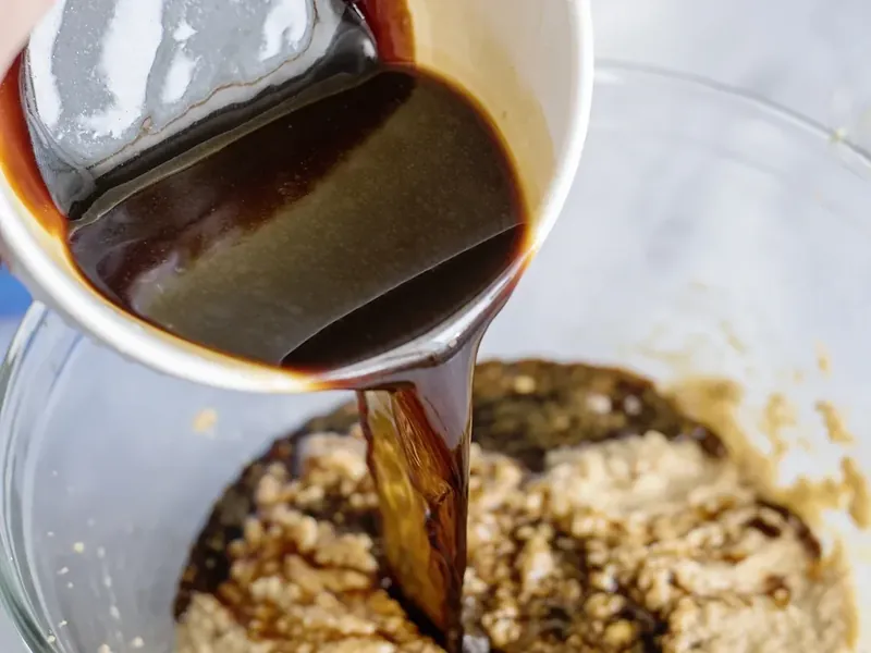 Dark molasses and hot water mixture being poured into butter and egg mixture