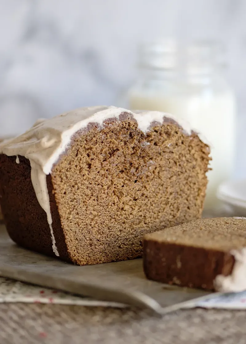 Single slice of glazed gingerbread loaf showing moist interior texture with glass of milk