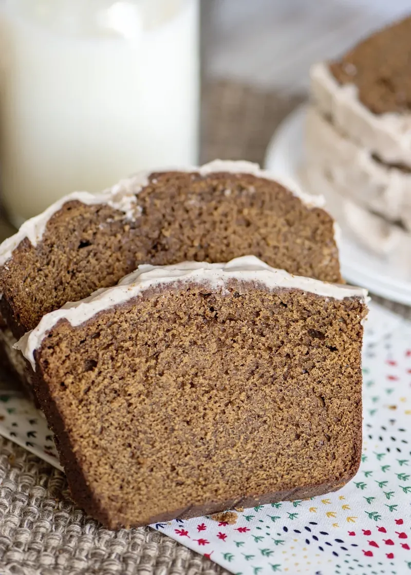 Sliced gingerbread loaf with glaze on rustic burlap cloth with cinnamon sticks and milk glass