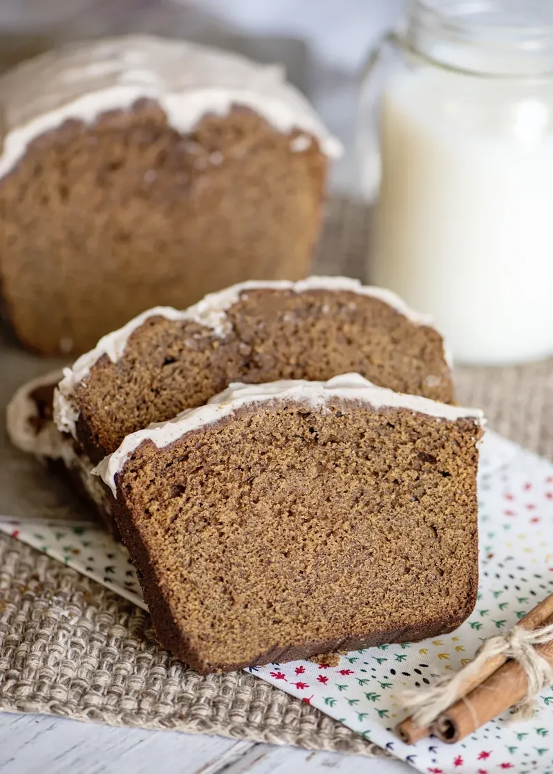 Sliced gingerbread loaf with white cinnamon glaze dripping down sides on cooling rack