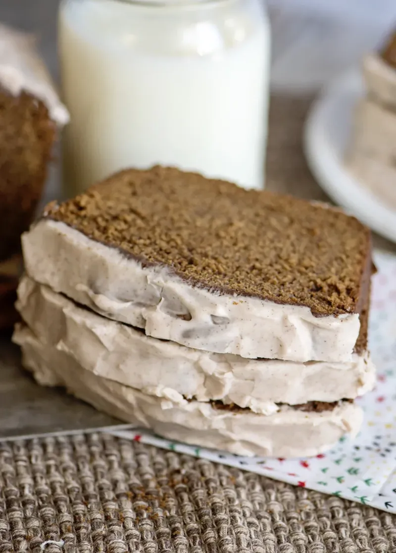 Multiple thick slices of glazed gingerbread loaf arranged on burlap with festive napkin
