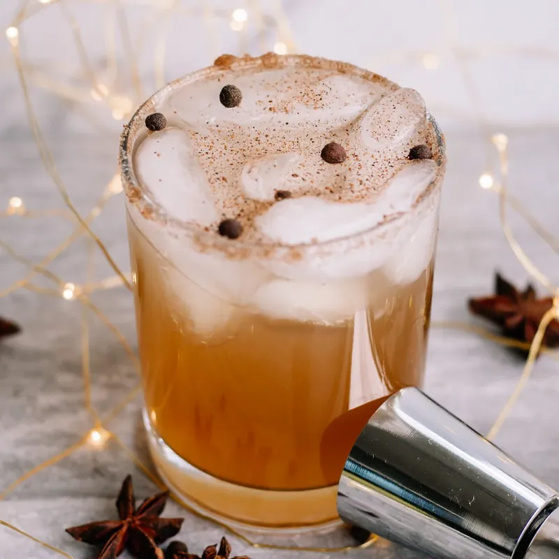 Beautiful gingerbread margarita with golden layers, spiced rim, and holiday lighting background