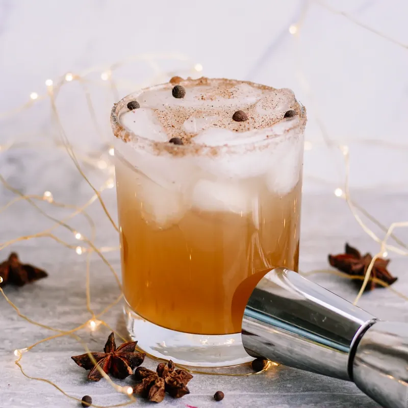 Side view of gingerbread margarita showing layered golden amber color with foam and spice garnish