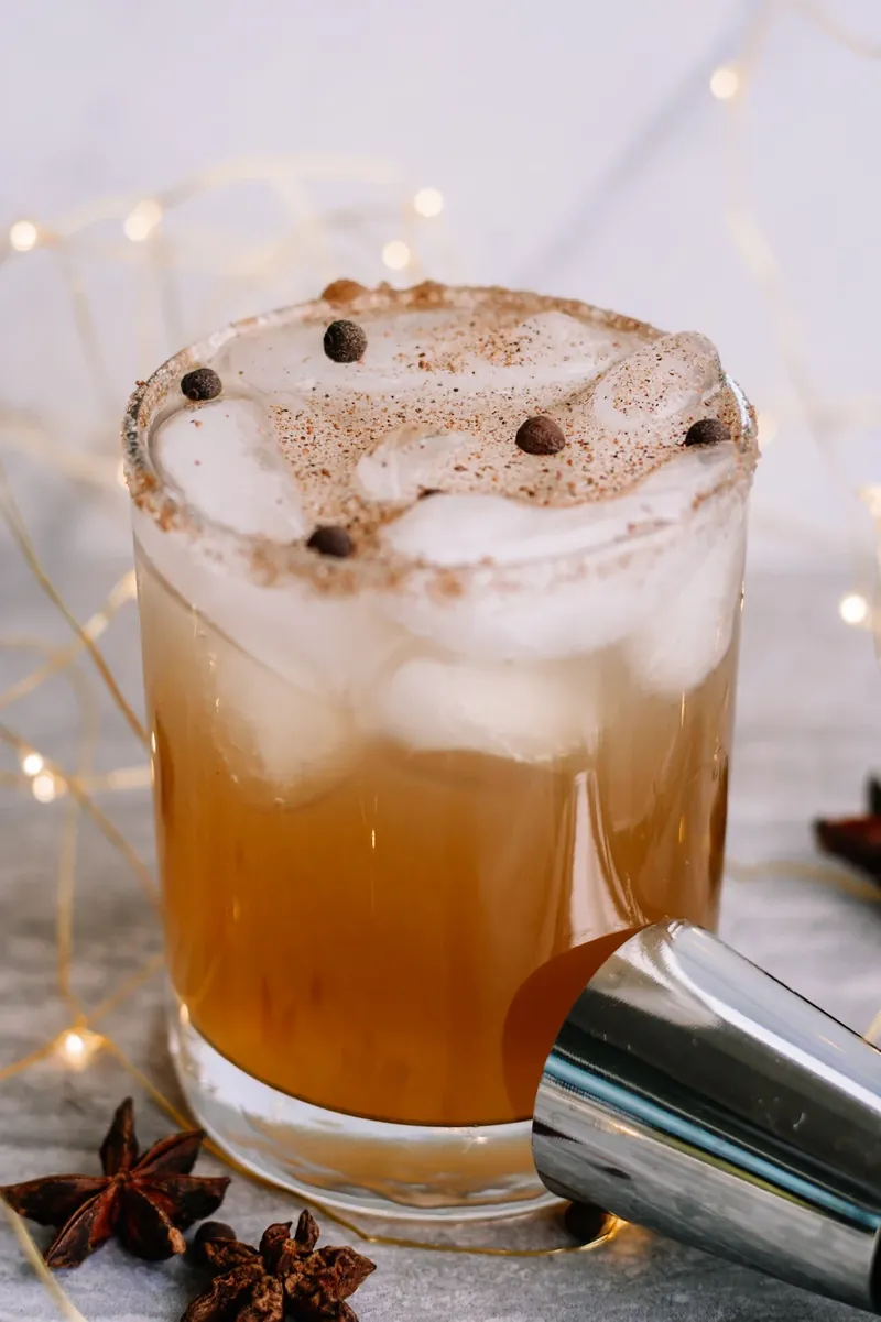 Golden gingerbread margarita with cinnamon sugar rim and allspice garnish on white background with fairy lights