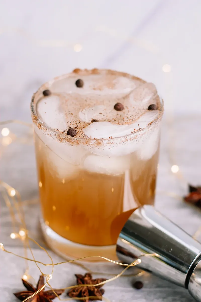 Layered gingerbread margarita showing golden amber color with foam top and allspice berries