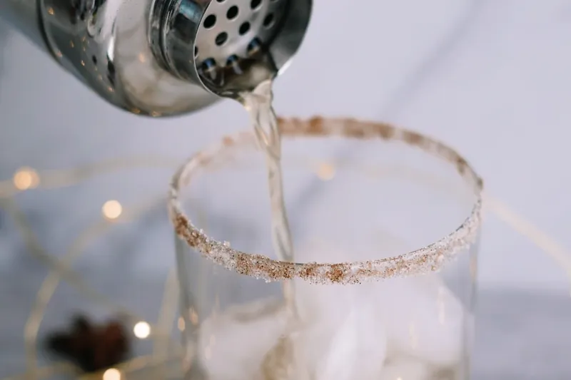 Pouring gingerbread margarita mixture from shaker into glass with cinnamon sugar rim